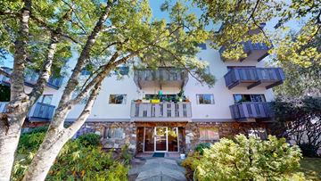 Victoria apartment for rent - A modern house with a stone facade and balconies surrounded by trees.