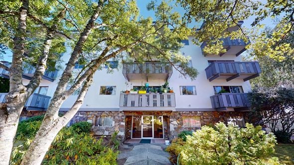 Victoria apartment for rent - A modern house with a stone facade and balconies surrounded by trees.