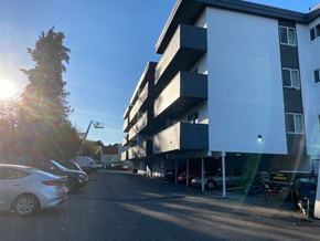 Victoria apartment for rent - A sunny day at a parking lot with cars and a building.