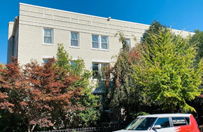 Washington apartment for rent - A red car is parked in front of a grey building with trees in the background.