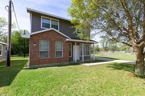 Prairie View apartment for rent - A house with a grey roof and a brick facade is surrounded by a grassy lawn.