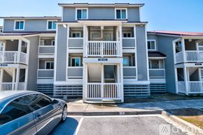 Folly Beach condo for rent - A silver car is parked in front of a grey apartment building.
