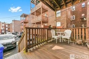 Brookline apartment for rent - A wooden deck with chairs and a table is in front of a brick building.
