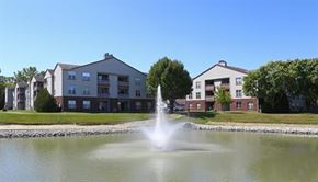 Buffalo Grove apartment for rent - A fountain in the middle of a pond in front of apartment buildings.