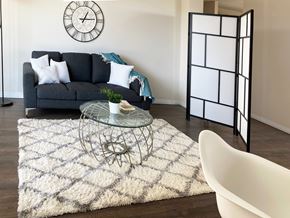 Edmonton apartment for rent - A living room with a grey sofa, a glass table, a white chair, a black and white clock, and a black folding screen.