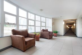 Burnaby apartment for rent - A long hallway with brown chairs and plants on either side.