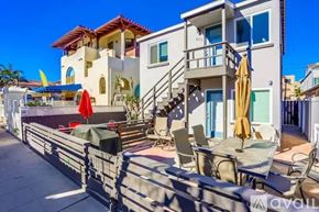 San Diego condo for rent - A modern two-story house with a balcony and a patio with chairs and umbrellas.