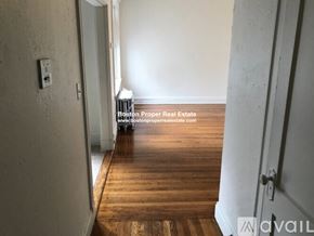 Boston apartment for rent - A room with wooden flooring and white walls, with a door on the left and a wall-mounted light fixture.