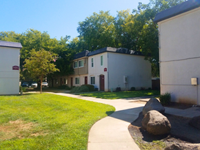 Rancho Cordova apartment for rent - A white building with a red door is surrounded by trees and a grassy area.