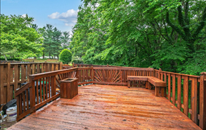 Bowie house for rent - A wooden deck with benches and a table surrounded by trees.