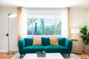 Joshua Tree house for rent - A green couch with two pillows sits in front of a window with a view of trees and mountains.