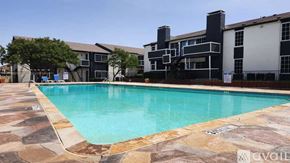 Dallas apartment for rent - A swimming pool surrounded by a stone patio and a building in the background.