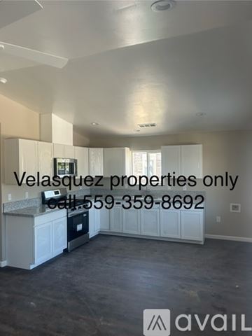 Porterville house for rent - A spacious, empty room with a kitchen area and a phone number for Velasquez properties.