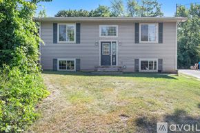 Kalamazoo house for rent - A house with a grey siding and a black door is surrounded by greenery.