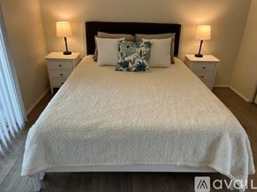 Oceanside house for rent - A bed with a white comforter and a black headboard with two lamps on the side tables.