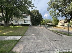 Pennsauken apartment for rent - A residential street with a white house on the left and a tree-lined sidewalk.