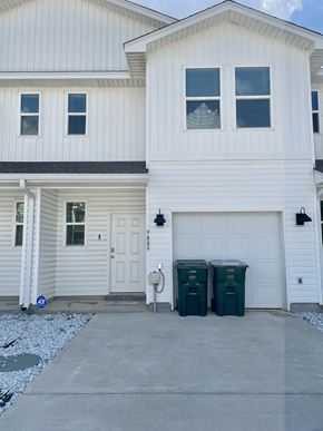 Pensacola townhouse for rent - A white house with a garage and two green bins in front.