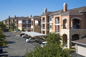 Austin apartment for rent - A parking lot with cars and a building with arches in the background.