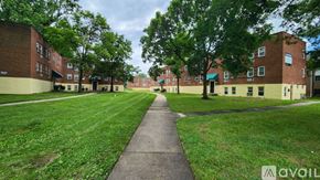 Baltimore apartment for rent - A grassy area with a walkway separates two rows of red brick apartment buildings.