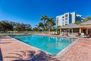 Bradenton house for rent - A large swimming pool surrounded by a brick patio with people relaxing in the background.