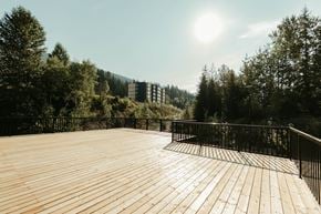 Revelstoke apartment for rent - A wooden deck with railings overlooks a forest and a building in the distance.