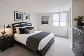 Scranton apartment for rent - A bedroom with a large bed, a nightstand with a lamp, and a dresser with a plant on top.