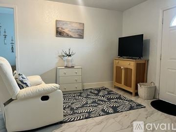 Bradenton apartment for rent - A living room with a white chair, a wooden cabinet, and a painting on the wall.