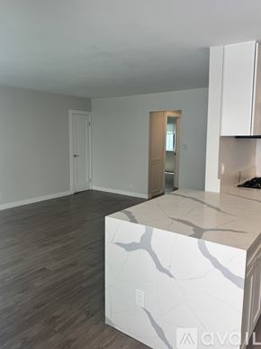 Santa Monica apartment for rent - A white kitchen island with a marble top is in the foreground of an empty room with wood flooring and white walls.