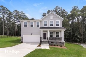 Four Oaks house for rent - A two-story house with a garage is surrounded by a grassy lawn and trees.