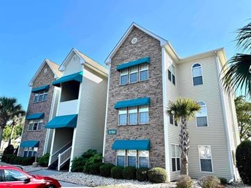 Myrtle Beach house for rent - A red car is parked in front of a two-story building with a stone facade and a blue awning.