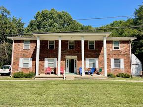 Louisville apartment for rent - A red brick house with a white porch and a white car parked in front.