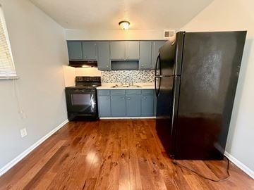 Louisville apartment for rent - A black refrigerator stands in a kitchen with wooden floors and grey cabinets.