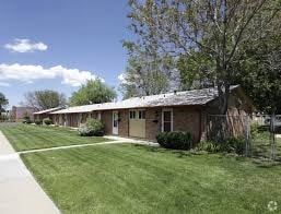 Denver apartment for rent - A small building with a brown roof is surrounded by a green lawn.