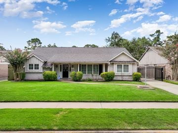 Houston house for rent - A house with a grey roof and white walls is surrounded by a green lawn.