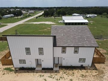Bastrop house for rent - A white two-story house with a black roof and a garage is surrounded by a dirt lot.
