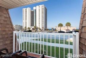 Daytona Beach apartment for rent - A balcony with a white railing overlooks a beach and buildings.