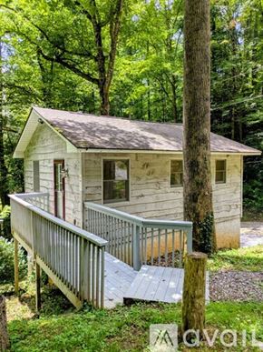 Sylva apartment for rent - A small white house with a porch is surrounded by trees.