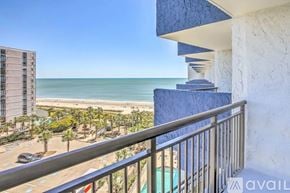 Myrtle Beach condo for rent - A balcony overlooks a beach with a building and palm trees in the distance.