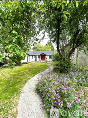 Portland house for rent - A small house with a red door is surrounded by greenery and purple flowers.