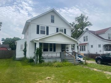 Lorain apartment for rent - A white house with a grey porch and a black car parked in front.