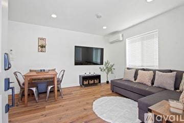 Placentia house for rent - A living room with a grey couch, a wooden dining table with chairs, a flat-screen TV, and a rug.