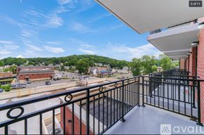 Peekskill apartment for rent - A balcony with a black railing overlooks a parking lot and buildings.