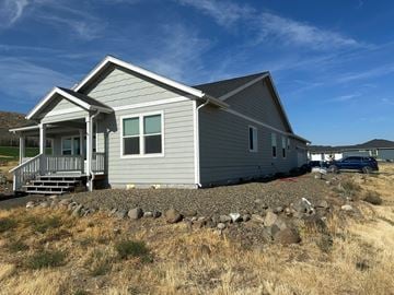Kennewick house for rent - A house with a grey siding and a porch is surrounded by rocks and grass.