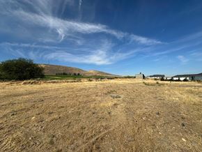 Kennewick house for rent - A barren landscape with a few buildings in the distance under a blue sky with clouds.
