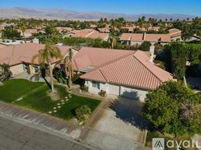 La Quinta house for rent - A house with a red tiled roof is surrounded by other houses and palm trees.
