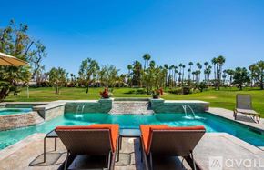 La Quinta house for rent - A pool with two lounge chairs and a table is surrounded by palm trees.