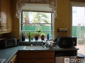 San Leandro house for rent - A kitchen with a sink, microwave, and window overlooking a green fence.
