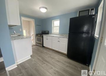 Pigeon house for rent - A kitchen with a black fridge, white cabinets, and a marble countertop.
