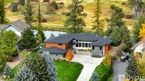Kalispell house for rent - A large house with a grey roof and a stone wall is surrounded by trees.