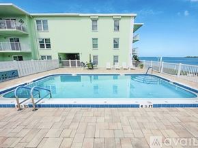 Dunedin apartment for rent - A pool in front of a light green building with a white fence around it.
